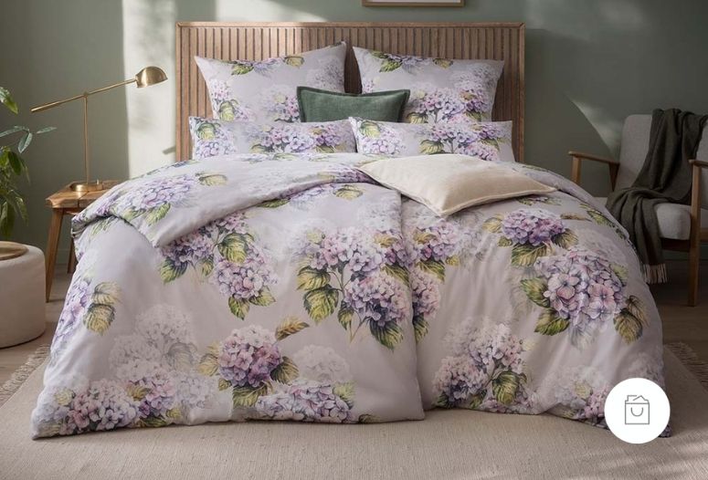 Satin de Luxe Bettwäsche mit großflächigem Hortensienmuster in der Farbe Flieder (zarte Lila-Rosé-Töne mit Grüntönen) arrangiert mit natürlicher Lichtstimmung. Demnächst verfügbar.
