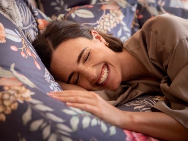 Frau liegt lächelnd im Bett - Bettbezug ist die floraler Bettwäsche Claudia in Blau.