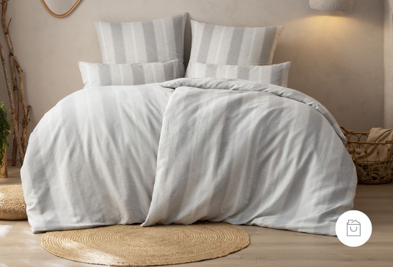 Bettwäsche aus Halbleinen mit feinen, weißen Streifen auf hellgrauem Grund – natürlicher Look, arrangiert in einem gemütlich eingerichteten Schlafzimmer.