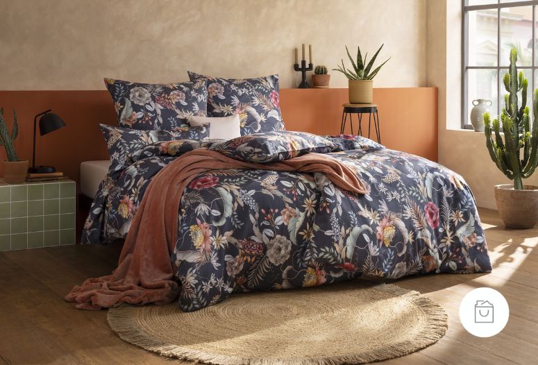 Bettwäsche Claudia mit üppigen Blüten, Blättern und Zweigen in Rosé-, Creme-, Gelb- und Grüntönen auf dunkelblauem Grund auf Bett im Schlafzimmer