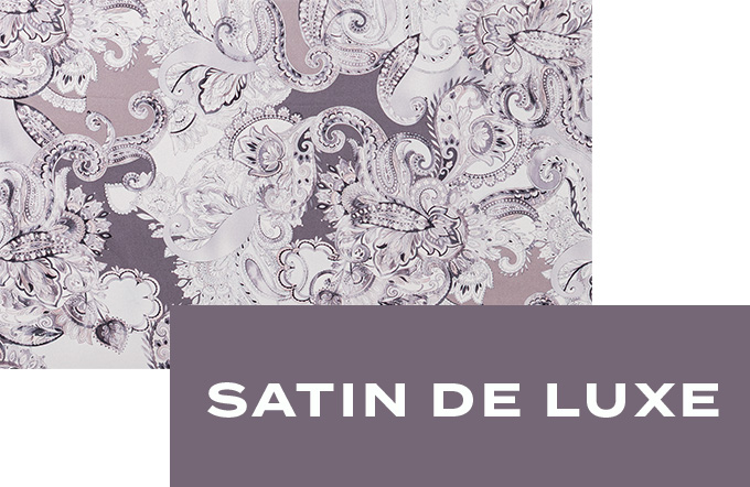 Nahaufnahme des glänzenden Satin de Luxe-Stoffs mit ornamentreichem Paisley-Muster in zarten Violett- und Beigetönen.