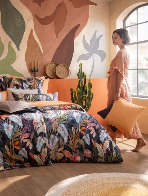 Bunte Bettwäsche Juliane mit tropischem Pflanzenmuster auf Doppelbett, kombiniert mit orangefarbener Bettwäsche Valetta und Dekokissen im Schlafzimmer.