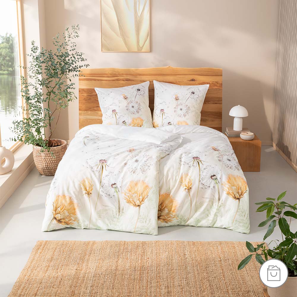 Bio-Bettwäsche mit floralem Löwenzahn-Motiv in hellen Farben in moderner Schlafzimmerumgebung.
