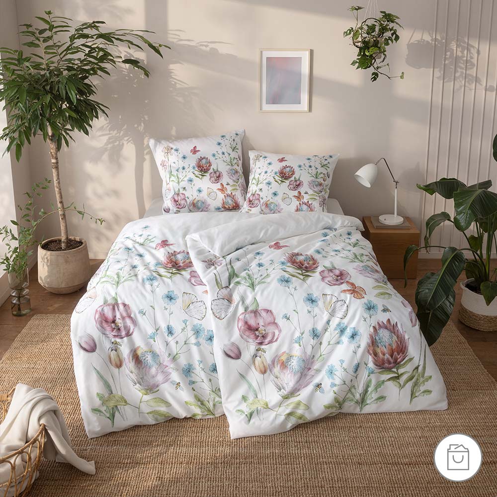 Bio-Bettwäsche mit zarten Blumen und Schmetterlingen in Rosa, Blau und Grün auf hellem Hintergrund in natürlicher Schlafzimmerumgebung.