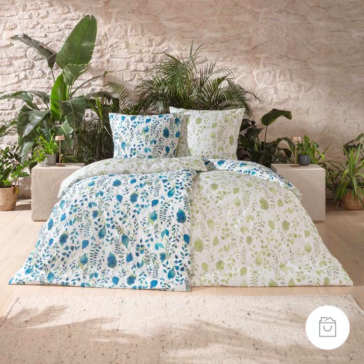 Bio-Bettwäsche Anabel als Wendebettwäsche mit Blättern in Blau und Grün auf weißem Grund auf Bett im Schlafzimmer