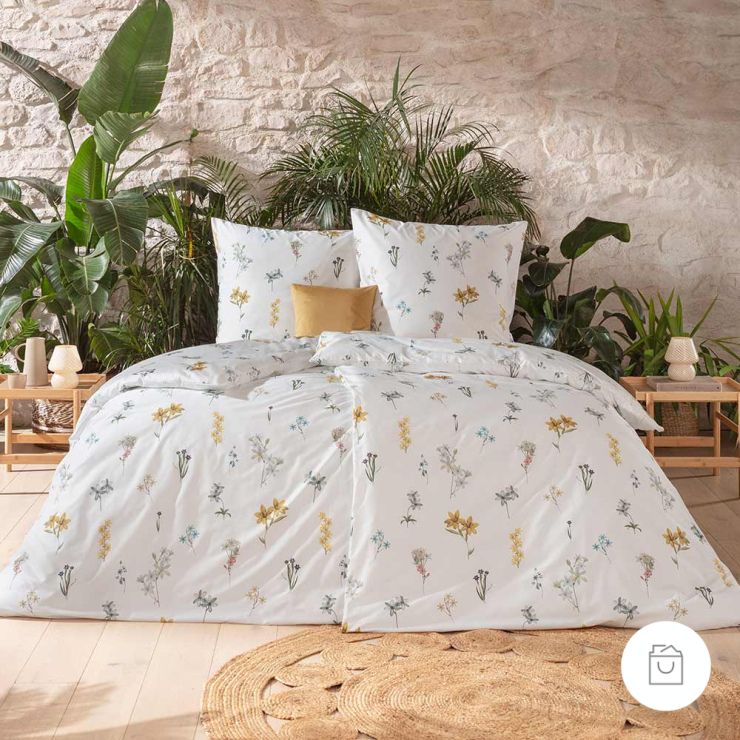 Bio-Bettwäsche Cintia mit zarten Wildblumen in Gelb, Rosa und Blau auf weißem Grund auf Bett im hellen Schlafzimmer