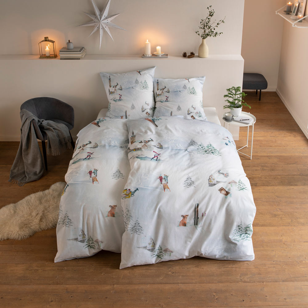 Bettwäsche St. Anton mit einem Winterlandschaftsmotiv auf weißem Grund auf Bett im Schlafzimmer
