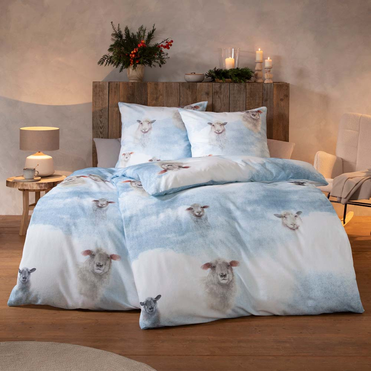 Bettwäsche Wilson mit Schafen in Grau und Weiß auf hellblauem Grund auf Bett im Schlafzimmer