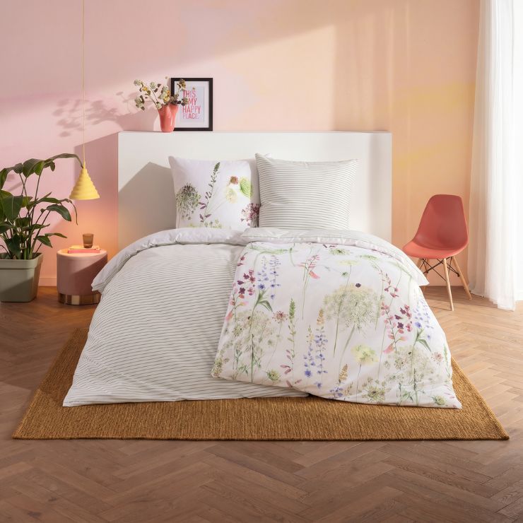 Bettwäsche Meadow als Wendebettwäsche mit Wiesenblumen in Grün und Lila sowie Streifen in Grau auf weißem Grund auf Bett im Schlafzimmer