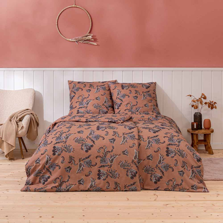 Bettwäsche Ostana mit dekorativem Paisley-Muster aus geschwungenen Blattformen und floralen Ornamenten in warmen Terrakotta-, Blau- und Cremetönen auf Bett im Schlafzimmer