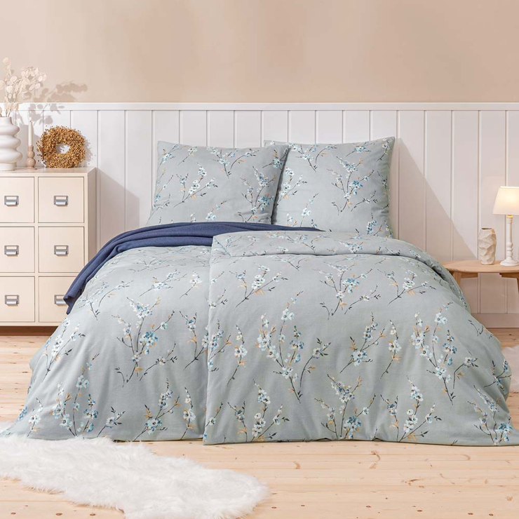 Bettwäsche Trento mit Blütenzweigen in Weiß und Blau auf hellgrauen Grund auf Bett im Schlafzimmer