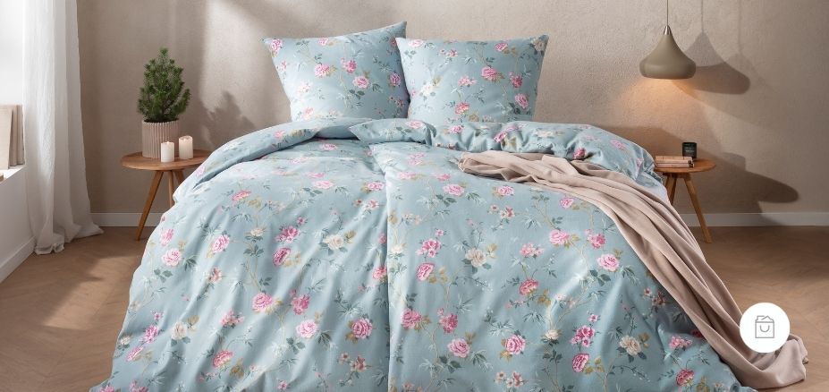 Bettwäsche Corvara mit zarten Rosenmotiven und feinen Ranken in Rosé, Creme auf sanftem blauen Grund auf Bett im Schlafzimmer