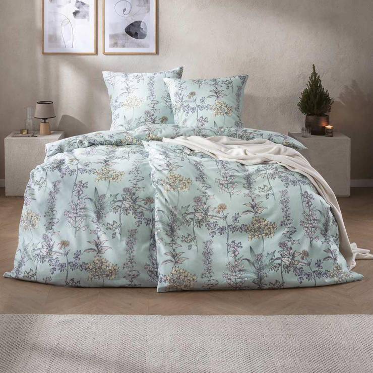 Bettwäsche Appiano mit feinen Wiesenblumen und filigranen Blütenzweigen in zarten Grün-, Lavendel- und Beigetönen auf hellem mintfarbenem Grund auf Bett im Schlafzimmer