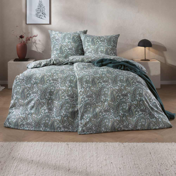 Bettwäsche Lagundo mit dichtem Paisley-Muster aus geschwungenen Ornamenten in kühlen Grün-, Blau- und Grautönen auf hellem Grund auf Bett im Schlafzimmer