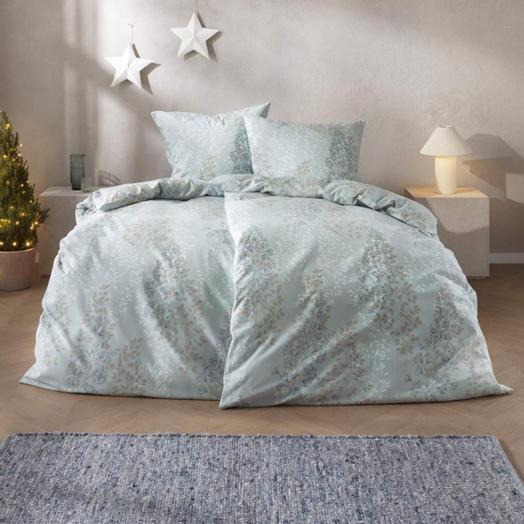 Bettwäsche Merano mit eleganten floralen Blattmotiven in sanften Blau-, Beige- und Grautönen auf hellem Grund auf Bett im Schlafzimmer
