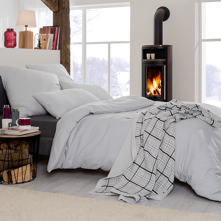 Bettwäsche Latemar in Uni-Optik mit feiner melierter Struktur in kühlen Grau- und Silbertönen auf Bett im Schlafzimmer