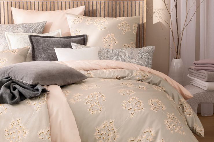 Bettwäsche Antje mit zartem Blütenmotiv in Beige, kombiniert mit unifarbener Bettwäsche Valetta, verschiedenen Dekokissen und Wohndecken auf Doppelbett in hellem Schlafzimmer