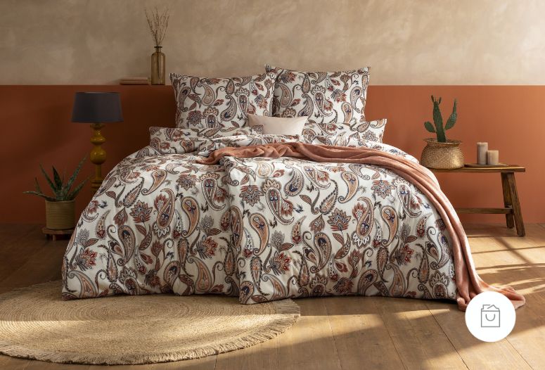 Bettwäsche Silke mit dekorativem Paisley-Muster aus geschwungenen Ornamenten und floralen Elementen in Terrakotta-, Blau- und Beigetönen auf beigem Grund auf Bett im Schlafzimmer