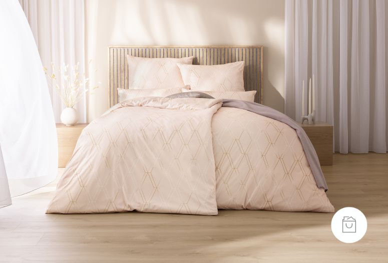 Bettwäsche Robert mit feinem geometrischem Rautenmuster aus goldenen Linien in zarten Rosé- und Beigetönen auf roséfarbenem Grund auf Bett im Schlafzimmer