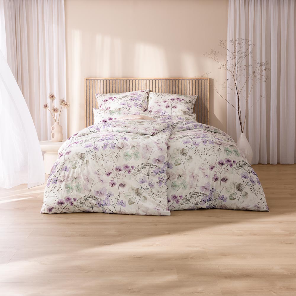 Bettwäsche Sonja mit Blumenmuster in Lila und Grün auf weißem Grund auf Bett im Schlafzimmer