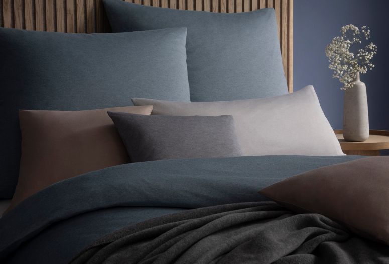 Mako-Interlock-Jersey-Bettwäsche Takoma in gedeckten Blau- und Grautönen auf Bett mit mehreren Kissen.