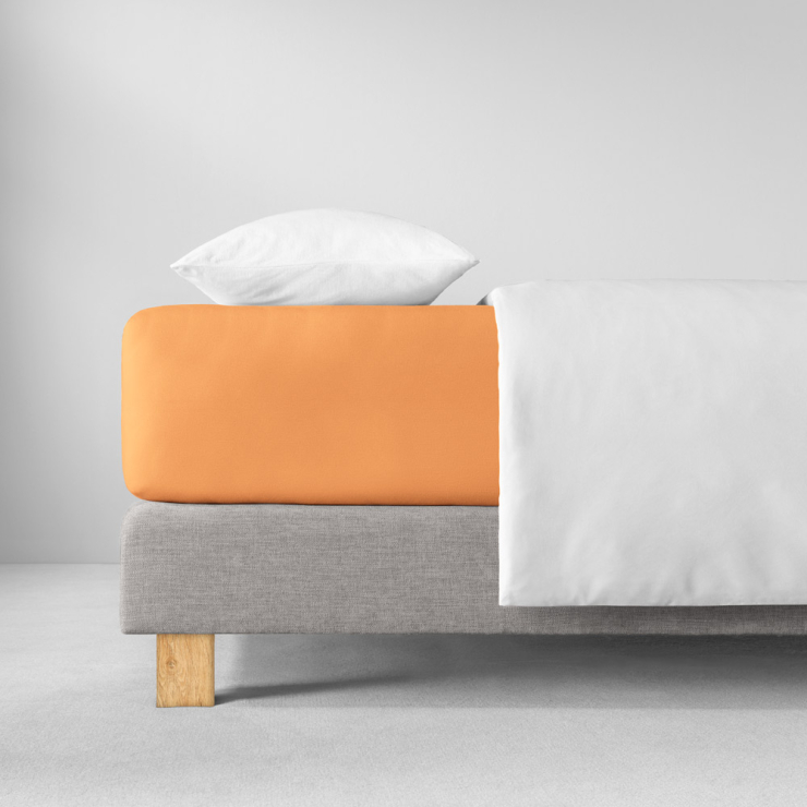 Spannbettlaken in hellen, pfirsichfarbenen Orangeton auf Bett aufgezogen