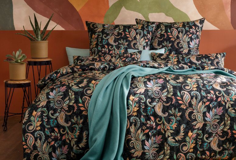 Bettwäsche Juliane mit floralem Muster auf dunklem Hintergrund, kombiniert mit uni Bettwäsche Valetta in azur und mehreren Dekokissen auf modernem Bett