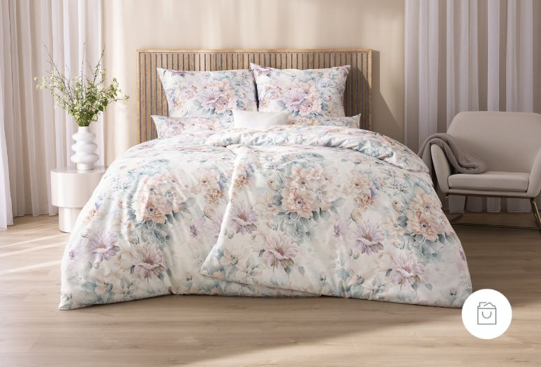 Bettwäsche Astrid mit großen, weich gezeichneten Blüten und feinen Blättern in Rosé-, Creme- und sanften Blautönen auf hellem Grund auf Bett im Schlafzimmer