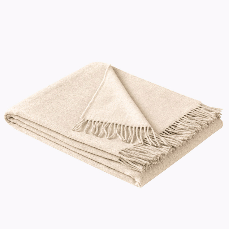 Gefaltete Wohndecke in Beige, ein warmer Naturton mit weicher Oberfläche und Fransen an der Kante