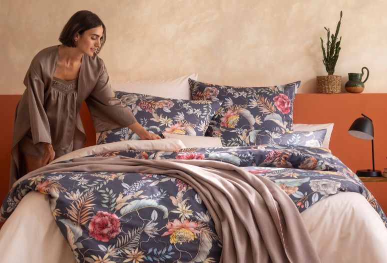 Frau richtet florale Bettwäsche Claudia in Blau, Rosé und Naturtönen auf Doppelbett, kombiniert mit Uni Bettwäsche Valetta in Puder und passender Wohndecke