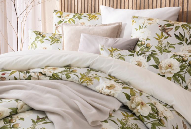 Florale Bettwäsche Yvonne in Beige mit weißen Blüten und grünen Blättern, kombiniert mit unifarbener Bettwäsche Valetta, Wohndecke Trevi und mehreren Dekokissen auf Doppelbett in hellem Schlafzimmer