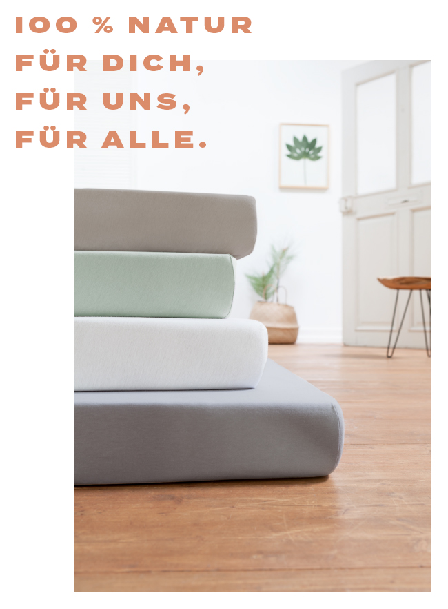 Gestapelte Bio-Spannbetttücher in 4 Naturtönen in modernem Raum mit Holzboden.