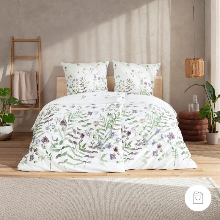 Bettwäsche Leticia mit Blüten und Blättern in Grün und Lila auf weißem Grund auf Bett im Schlafzimmer