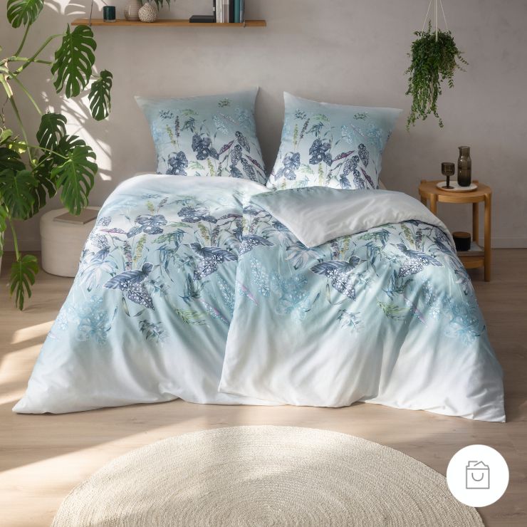 Bio-Bettwäsche Soraia in der Farbe Azur mit tropischem Blättermuster in Anthrazit, Eisblau und Violett auf fließendem Farbverlauf von weiß nach blau.