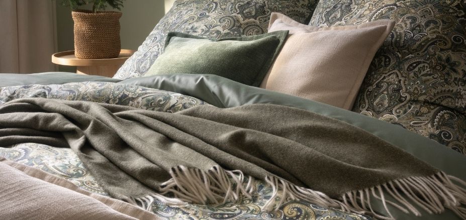 Bettwäsche Dunja mit Paisleymuster in Grün- und Beigetönen, kombiniert mit unifarbener Bettwäsche Valetta, verschiedenen Dekokissen und Wohndecken auf Doppelbett im Schlafzimmer