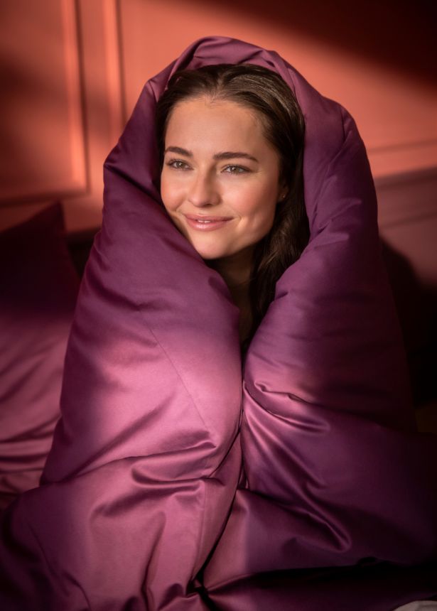 Moodbild: Frau kuschelt sich in lilafarabene Uni-Bettwäsche, vermittelt Wärme und Geborgenheit.