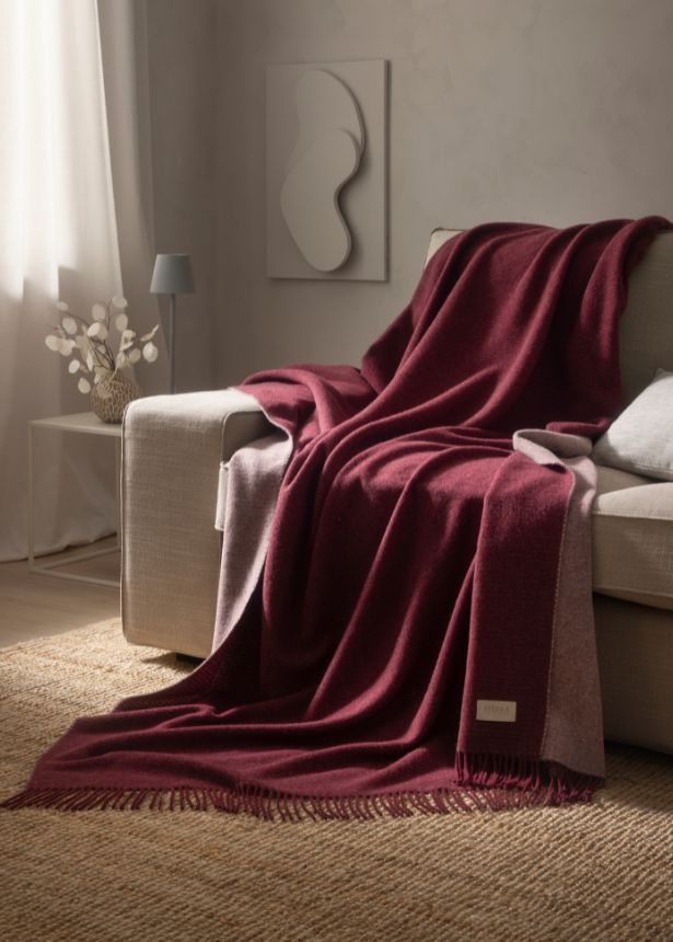 Wohndecke Eric in der Farbe vino auf Couch platziert für ein gemütliches Ambiente
