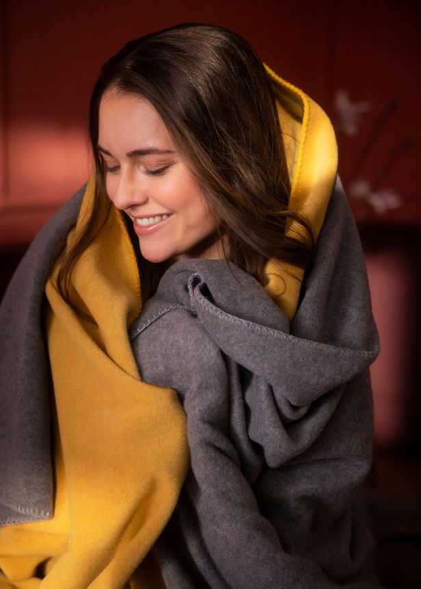 Frau kuschelt sich in gemütliche Kuscheldecken aus Fleece in Gelb und Grau.