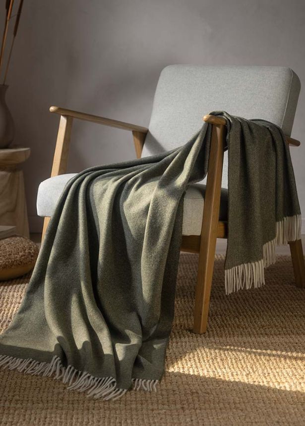 Estella Wohndecke Lana in der Farbe tanne (braun-grün-ton) gemütlich über Stuhl gelegt.