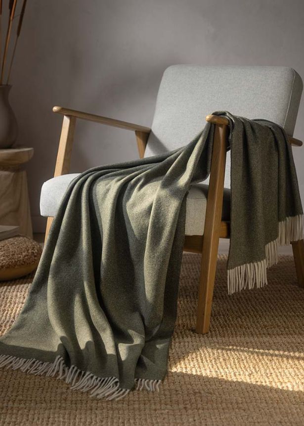 Wohndecke Lana in der Farbe tanne (helleres braun-grün) auf Stuhl platziert für ein gemütliches Ambiente