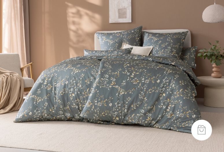 Bettwäsche Irma mit Blüten und Blättern in Beige und Weiß auf blauem Grund auf Bett im Schlafzimmer