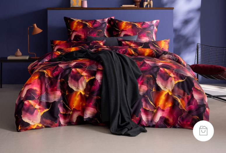 Bettwäsche Parzifal mit Blüten in kräftigen Rosa und Orange Tönen mit schwarzem Akzenten auf Bett im Schlafzimmer