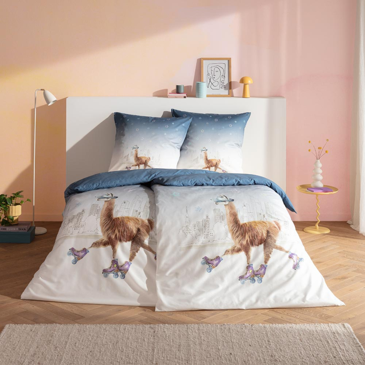 Bettwäsche City Lama mit Lama auf Rollschuhen und Sternen in Braun und Blau auf weißem Grund auf Bett im Schlafzimmer